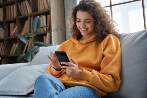 Happy teen girl checking social media holding smartphone at home. 